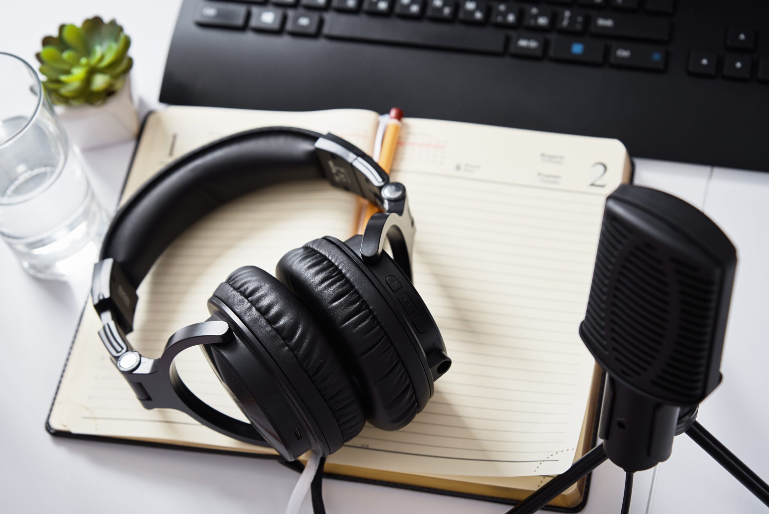 microphone and headphones on a table, notebook, keyboard also on table.