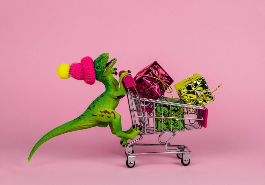 A dinosaur wearing a colourful hat, pushing a shoppin cart with gifts. An image headlining:Podcast Advertising Sold Me On It: What I Bought and Loved