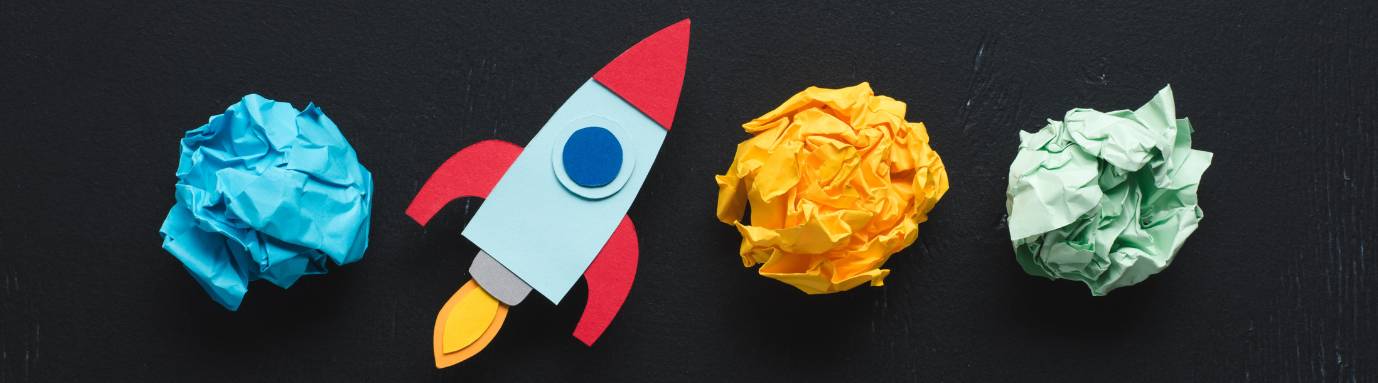 top view of cardboard rocket with crumpled paper balls on black background