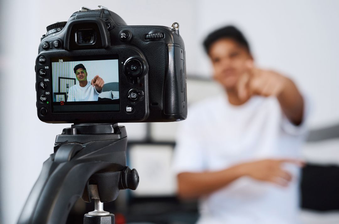 A blurred image of a male with short dark hair recording a video.