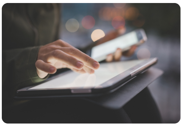 Person using a tablet and smartphone at night with blurred lights in the background.