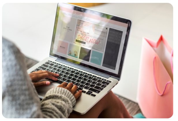 Person browsing an online store on a laptop with a shopping bag beside them.