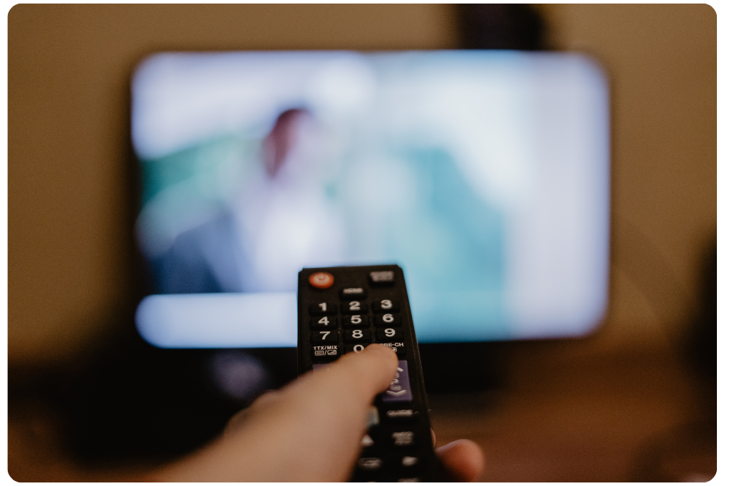 A person holding a TV remote while watching a blurred screen in the background, representing the rise of streaming and connected TV consumption.