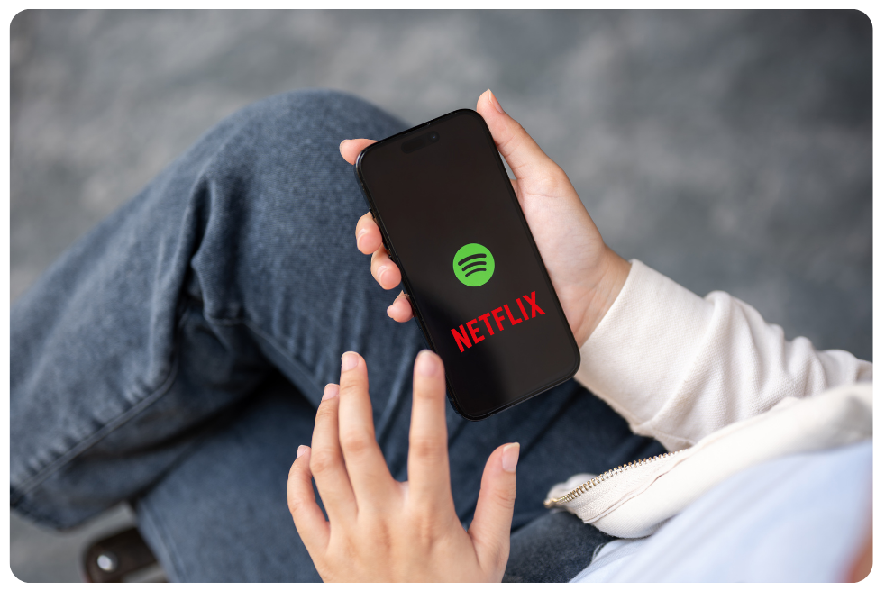 Person holding a smartphone displaying Spotify and Netflix logos, representing Spotify podcasts expanding to Netflix.