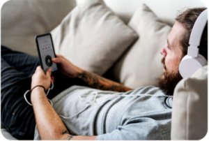 Man wearing headphones relaxing on a couch while listening to a podcast on his phone