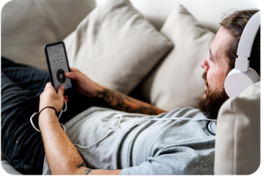 Man wearing headphones relaxing on a couch while listening to a podcast on his phone