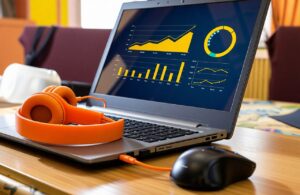 Laptop displaying podcast advertising performance charts and growth metrics, with orange headphones resting beside it on a desk.