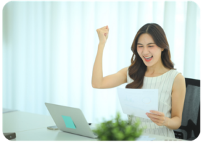 Woman at a desk celebrating with a raised fist while holding a printed report, with a laptop in front of her