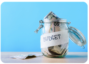 Glass jar labeled BUDGET filled with cash on a wooden surface