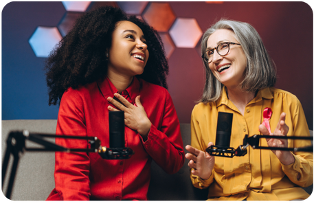 Two podcast co-hosts laughing together at the microphone during a recording session