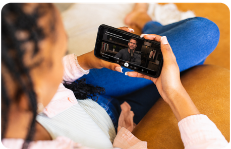 Listener relaxing on a couch watching a video podcast episode on her phone