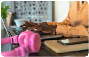 Woman working on a laptop with a smartphone beside her while reading the Signal Hill Insights 2026 Podcast Advertising Benchmark Report.