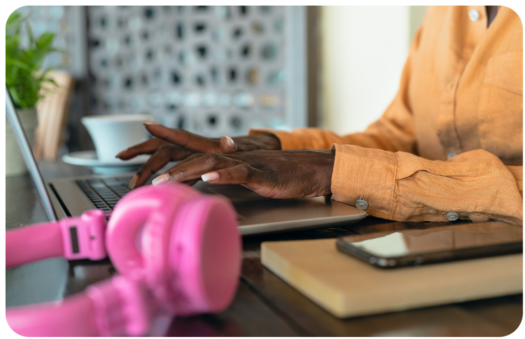 Woman working on a laptop with a smartphone beside her while reading the Signal Hill Insights 2026 Podcast Advertising Benchmark Report.