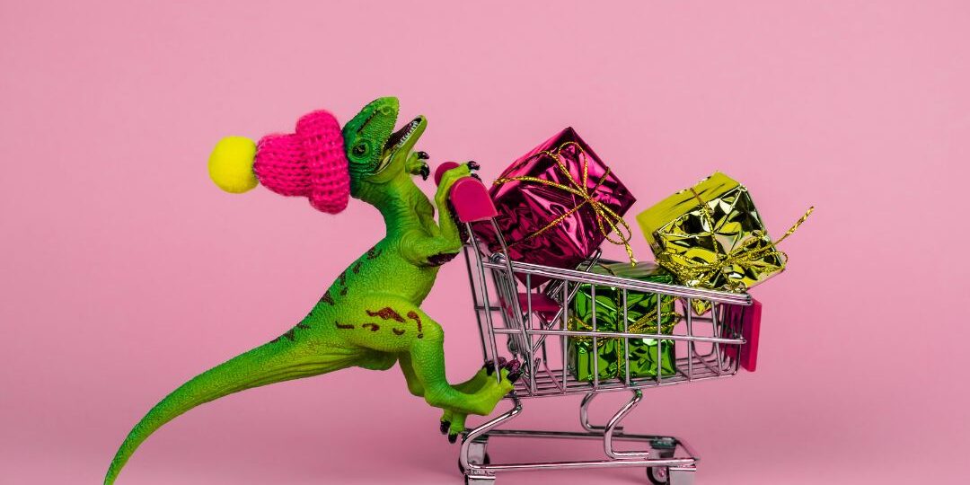 Playful green dinosaur character juggling pink raspberries and holding shopping cart filled with colorful gift boxes on pink background