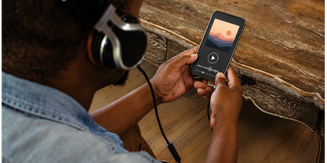 Person wearing over-ear headphones listening to a news podcast on a smartphone, illustrating how DTC brands are navigating podcast advertising during the 2026 midterm election ad spending surge