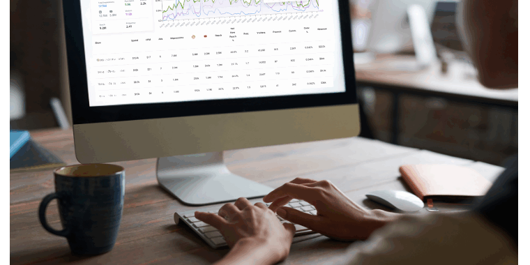 Hands on computer mouse at desk with analytics dashboard displaying podcast metrics, graphs, and performance data on monitor - representing podcast advertising measurement and campaign tracking