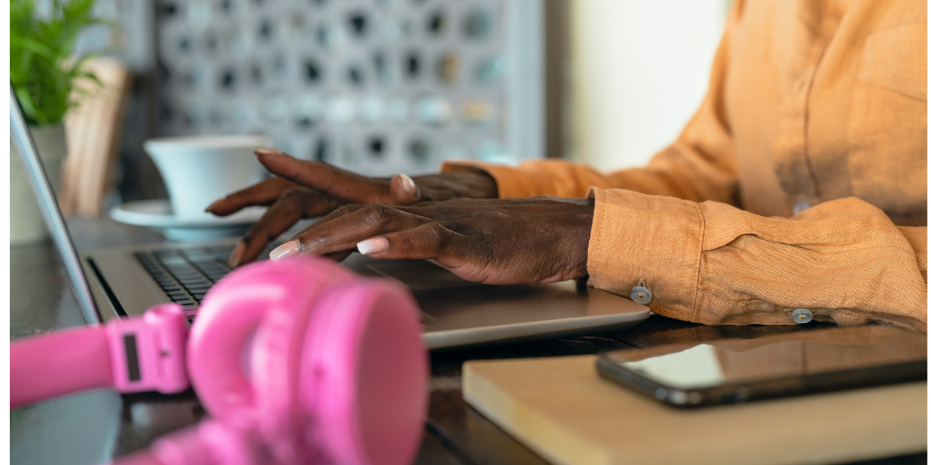 Woman working on a laptop with a smartphone beside her while reading the Signal Hill Insights 2026 Podcast Advertising Benchmark Report.