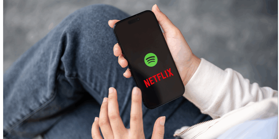 Person holding a smartphone displaying Spotify and Netflix logos, representing Spotify podcasts expanding to Netflix.