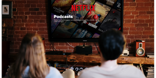 Two people watching a Netflix podcast on a large flat-screen TV in a modern living room