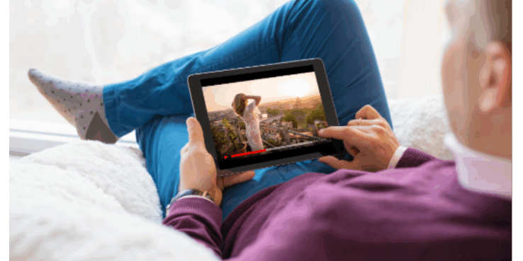 erson lying on bed wearing blue and purple clothing holding tablet displaying wildlife imagery, representing digital content consumption and YouTube sponsorship opportunities