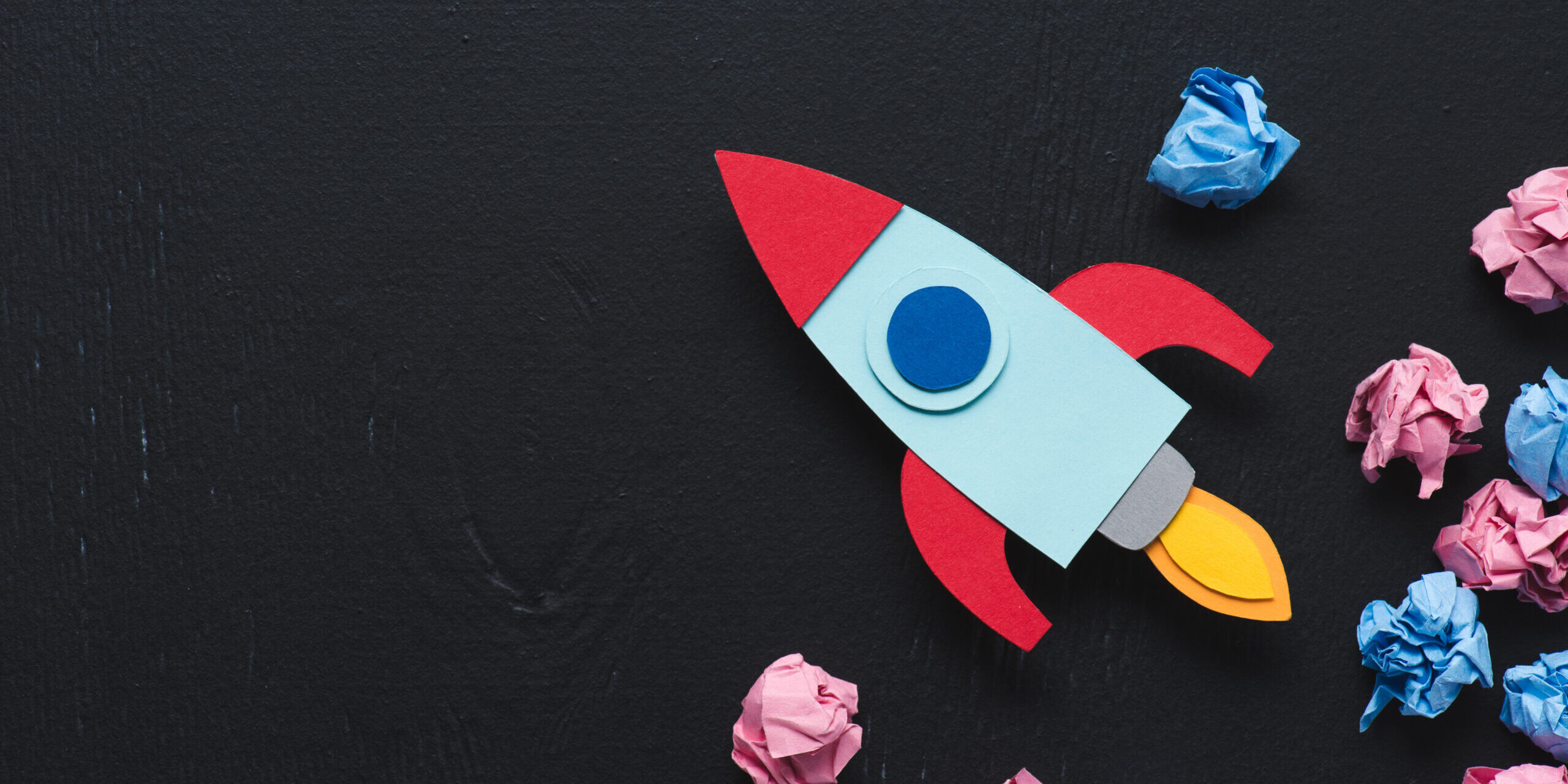 cardboard rocket with crumpled paper balls and copy space on black background, setting goals concept