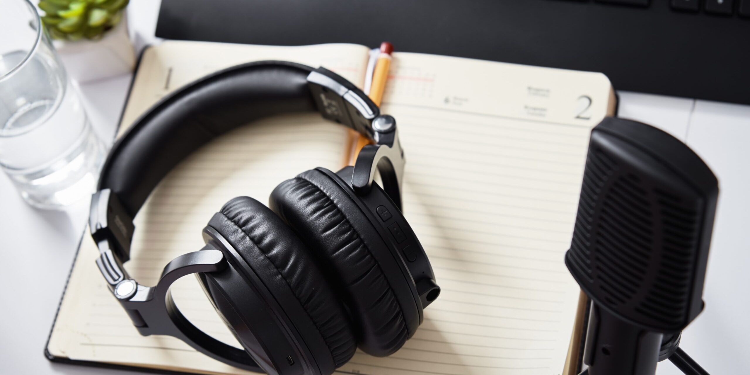 microphone and headphones on a table, notebook, keyboard also on table.