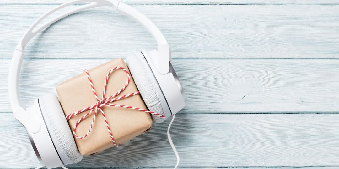White over-ear headphones embracing kraft paper gift box with red and white striped twine on light blue wooden background